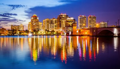 Multiple locations thrive in West Palm Beach, FL, where a vibrant skyline reflects off the waterfront, featuring modern high-rises, a lit bridge.